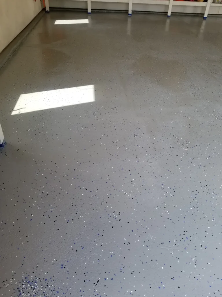 Gray epoxy-coated garage floor with blue and silver decorative flakes, sunlight reflecting off the smooth surface