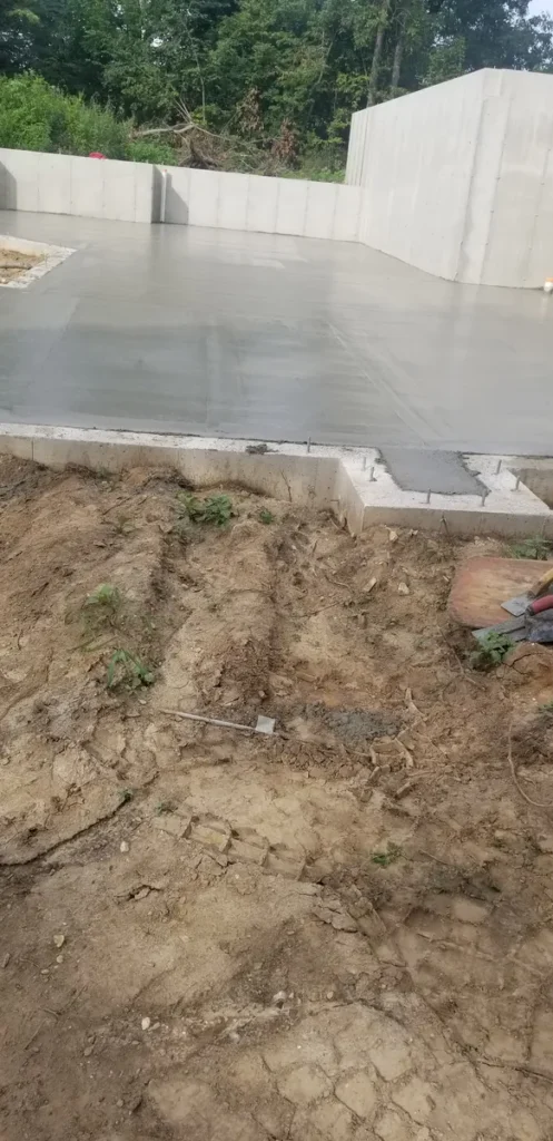 Freshly poured and smoothed concrete slab with concrete block retaining wall, surrounded by exposed dirt