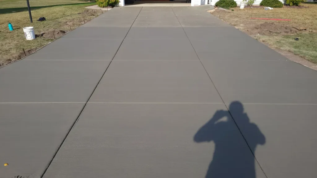 Newly poured concrete driveway with control joints leading to a two-car garage, photographer shadow visible in foreground
