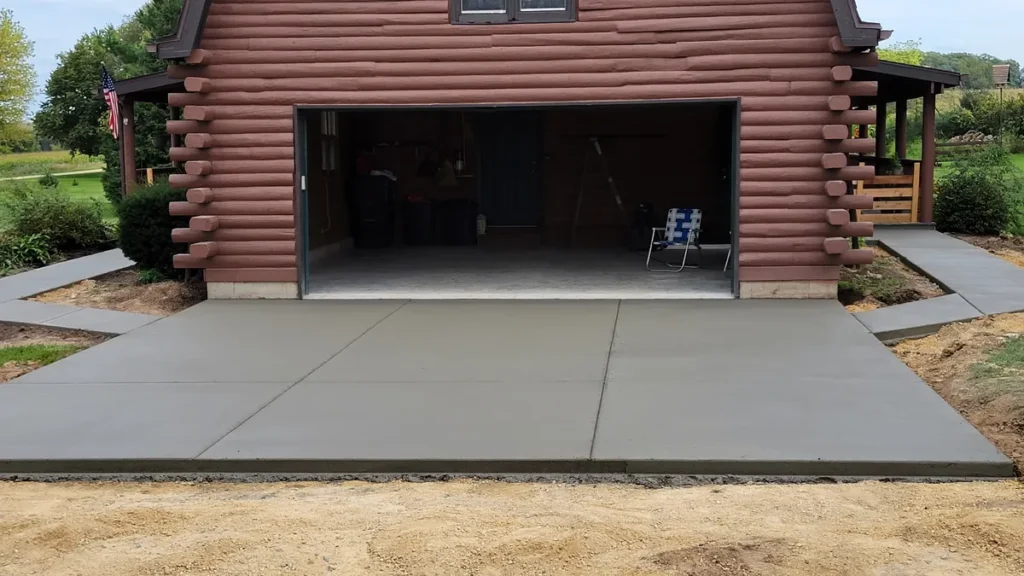 New concrete apron and pad poured in front of a log cabin garage with control joints visible