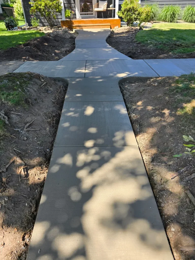 New concrete sidewalk with a T-shaped intersection leading to wooden front porch steps, dappled with tree shadows