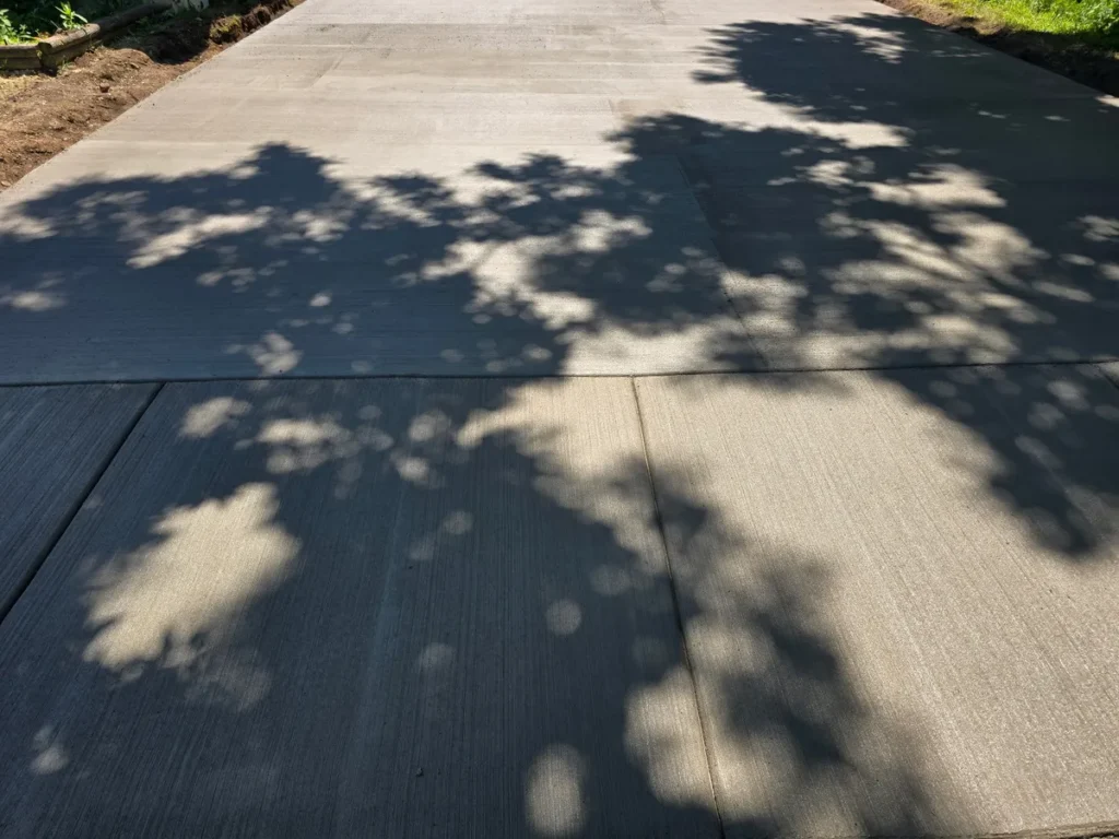 New concrete driveway with brushed finish and control joints covered in dappled tree shadows