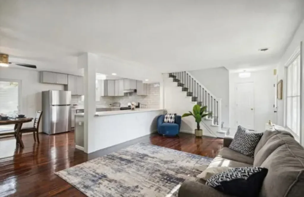 Open-concept living room and kitchen renovation with hardwood floors, gray cabinets, marble-look countertop, and a staircase
