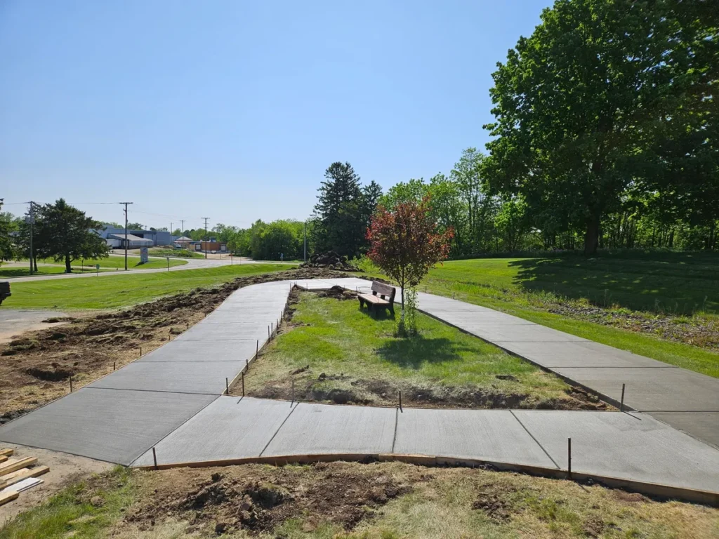 Two parallel concrete sidewalk paths curving around a landscaped island with a bench and shade tree