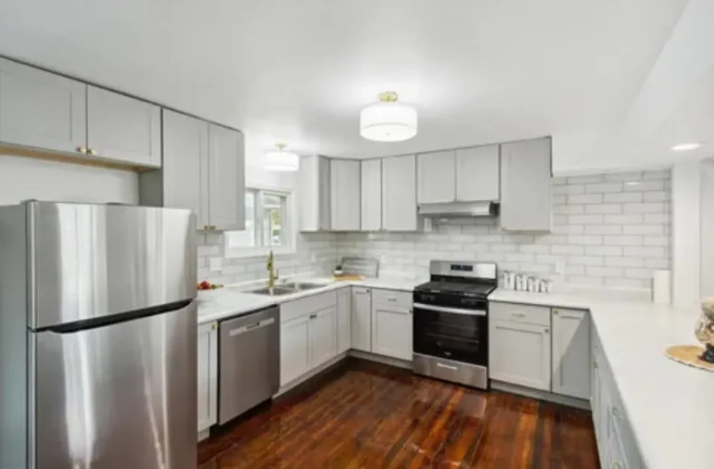 Finished kitchen renovation with gray shaker cabinets, white quartz countertops, subway tile backsplash, and stainless steel appliances