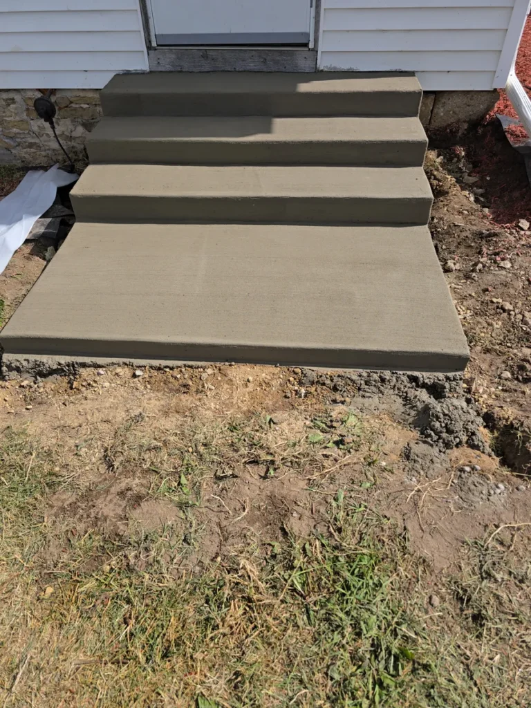 Newly poured concrete entry steps leading to a house door, surrounded by exposed dirt