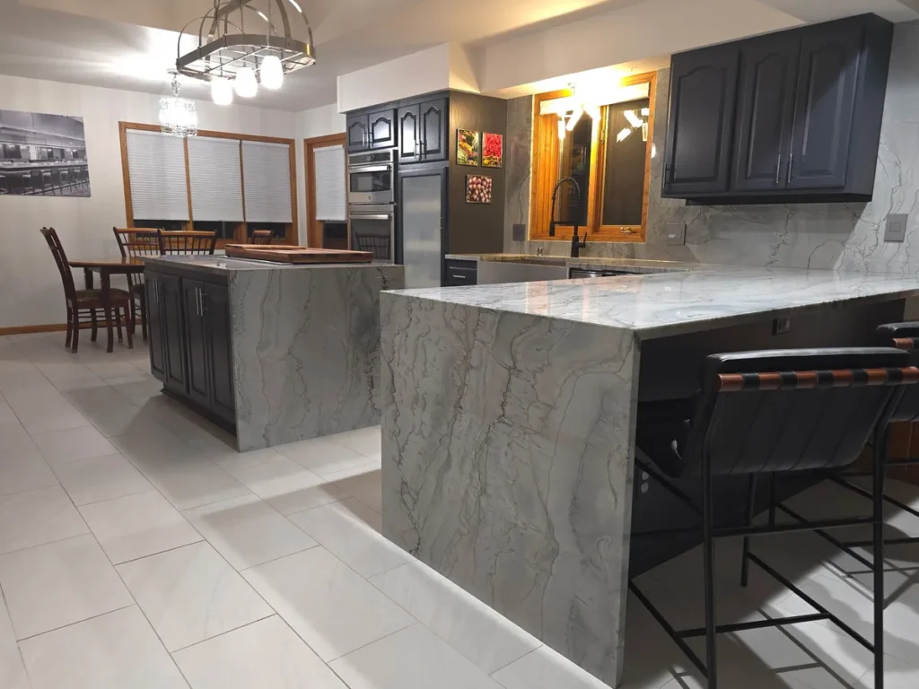 Modern kitchen with dark navy cabinets and a dramatic white marble-look quartz waterfall island countertop with bar stools