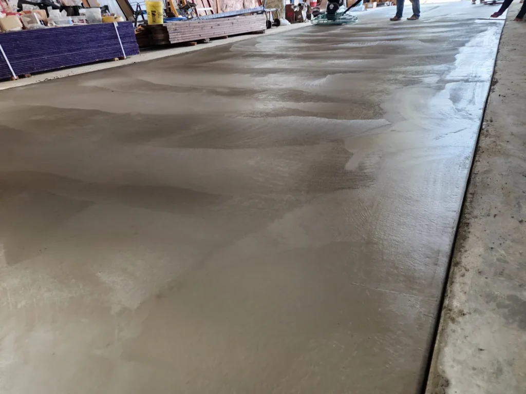 Freshly poured and hand-finished concrete floor inside a barn, smooth wet surface reflects the space