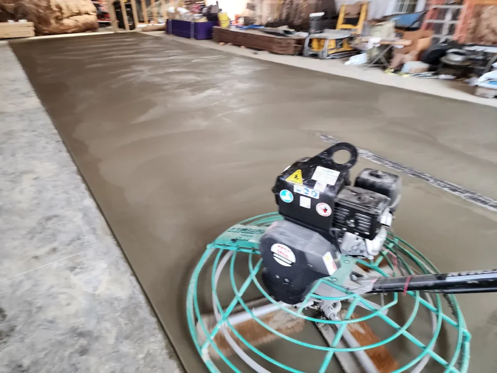 Power trowel machine in the foreground being used to finish a freshly poured concrete floor inside a commercial building
