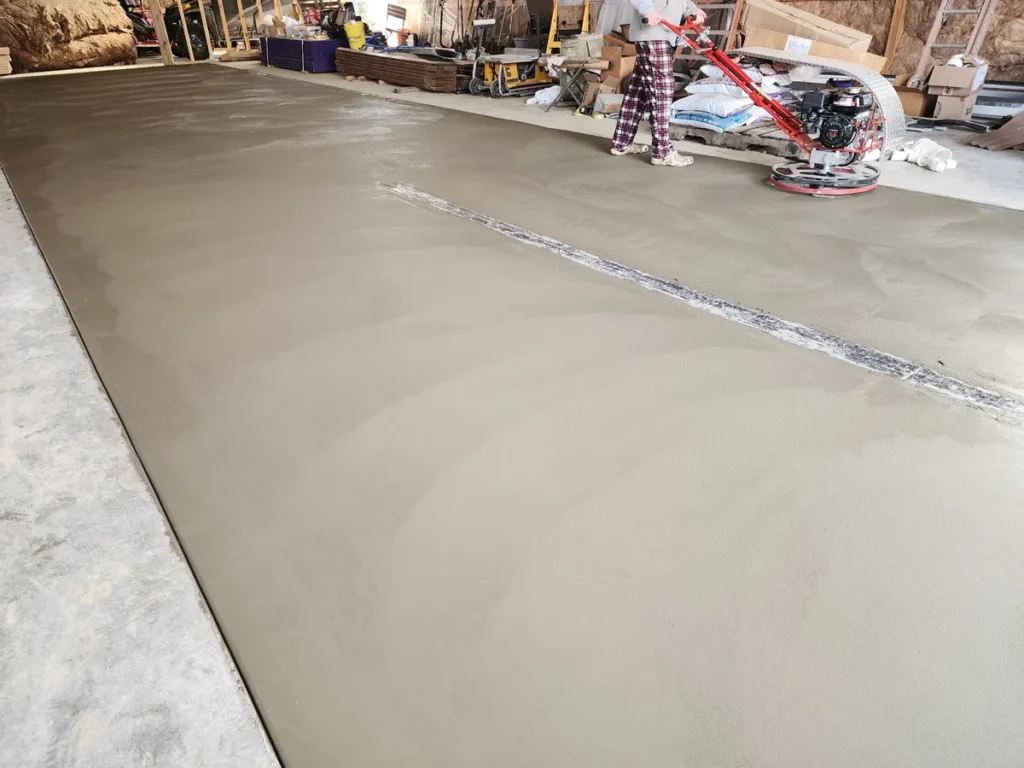 Freshly power-troweled concrete floor inside a barn with a red trowel machine visible in the background